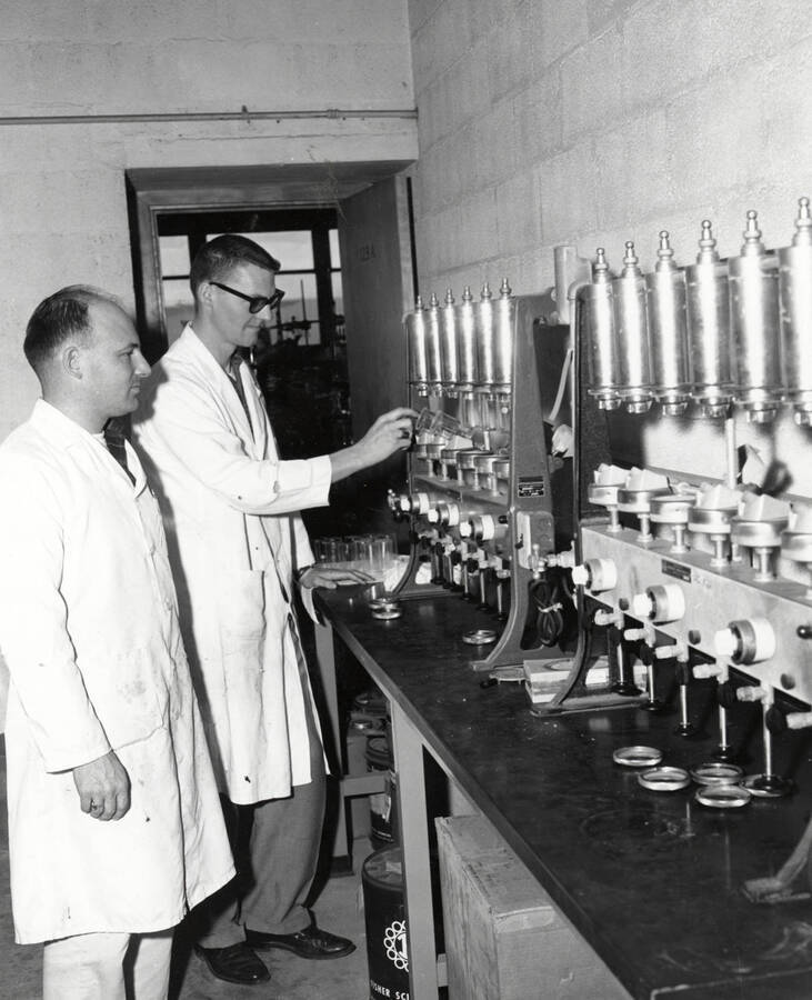 1961 photograph of Agricultural chemistry building. Professor and student work with equipment. [PG1_216_13]