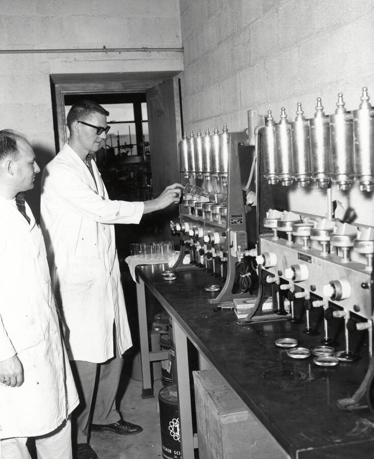1961 photograph of Agricultural chemistry building. Professor and student work with equipment. [PG1_216_14]