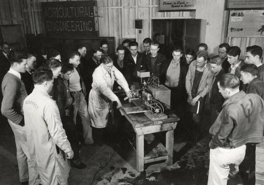 1928 photograph of Agricultural engineering building. Professor demonstrates the equipment to students in the shop. [PG1_217_07]