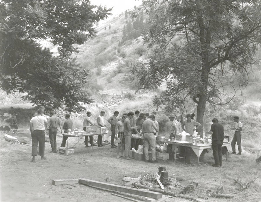 1968 photograph of College of Forestry. Students gather around tables near a camp fire during the forestry summer camp. Also print. Donor: Fred Johnson. [PG1_218-70a]