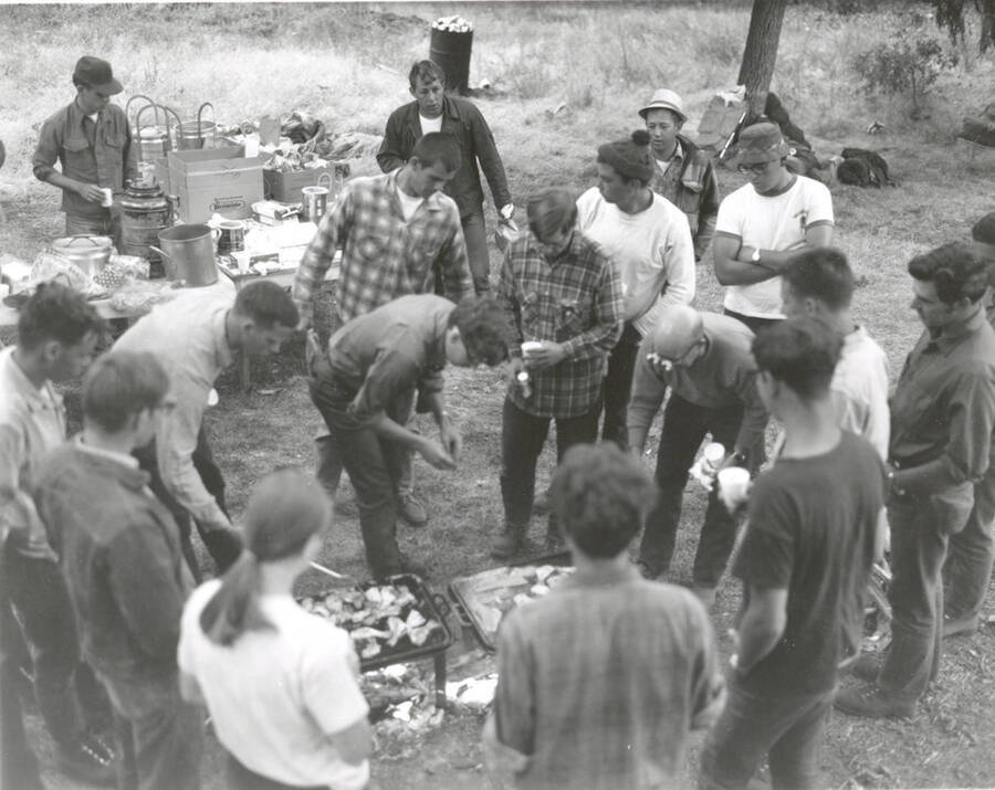 1969 photograph of College of Forestry. Students gather around trays of food at the campsite during the forestry summer camp. Also print. Donor: Fred Johnson. [PG1_218-71b]