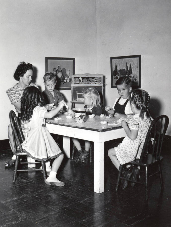 August 8, 1942 photograph of Home Economics. A student and five children sitting at a table during pre-school at Moscow High. [PG1_221-111a]
