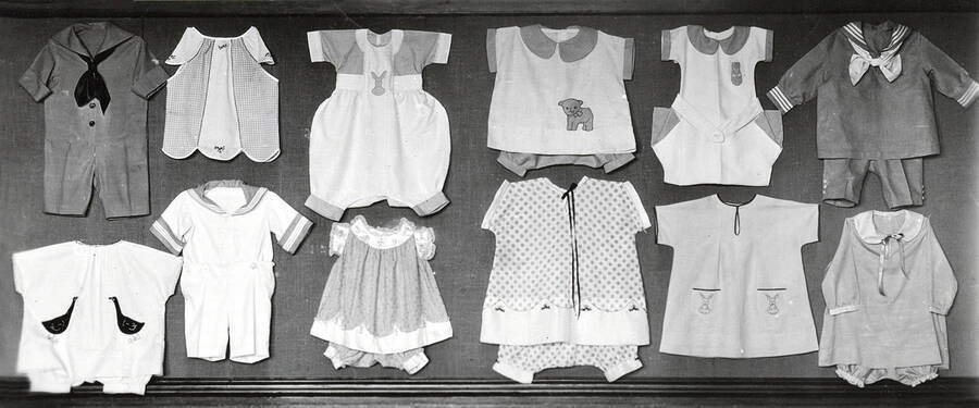 1928 photograph of Home Economics. Children's clothing pinned to a wall for an exhibt. [PG1_221-013]
