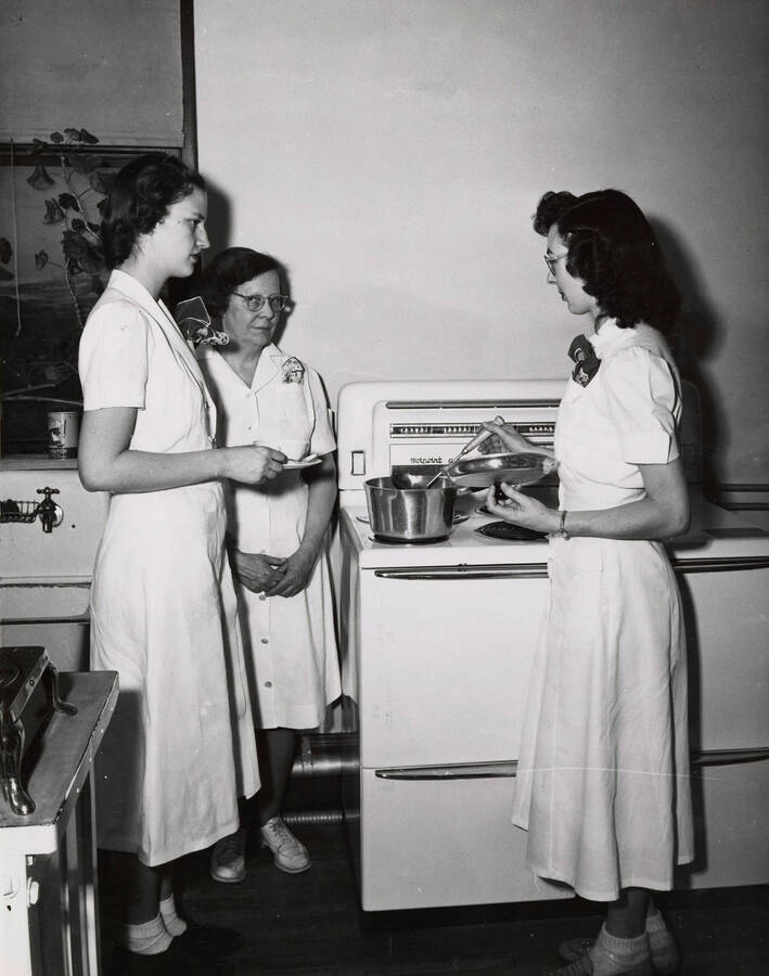 1945 photograph of Home Economics. Students gather around a stove during cooking class. [PG1_221-020]
