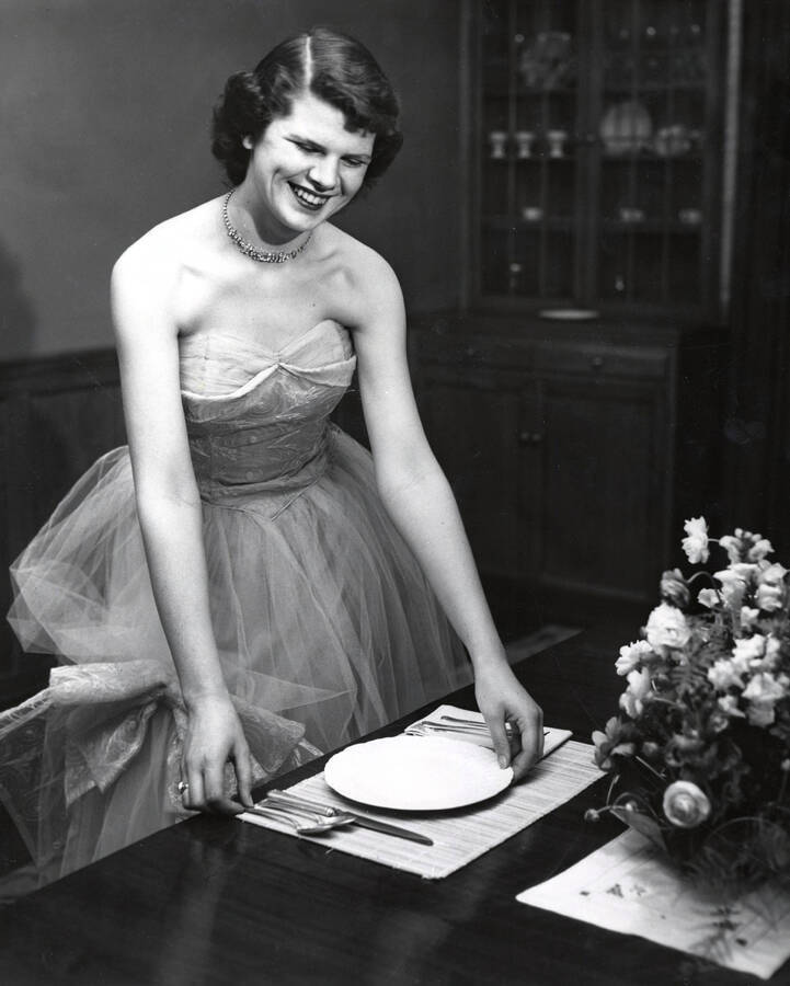 1948 photograph of Home Economics. A student in a cocktail dress arranges a place setting. Donor: Publications Dept. [PG1_221-043]