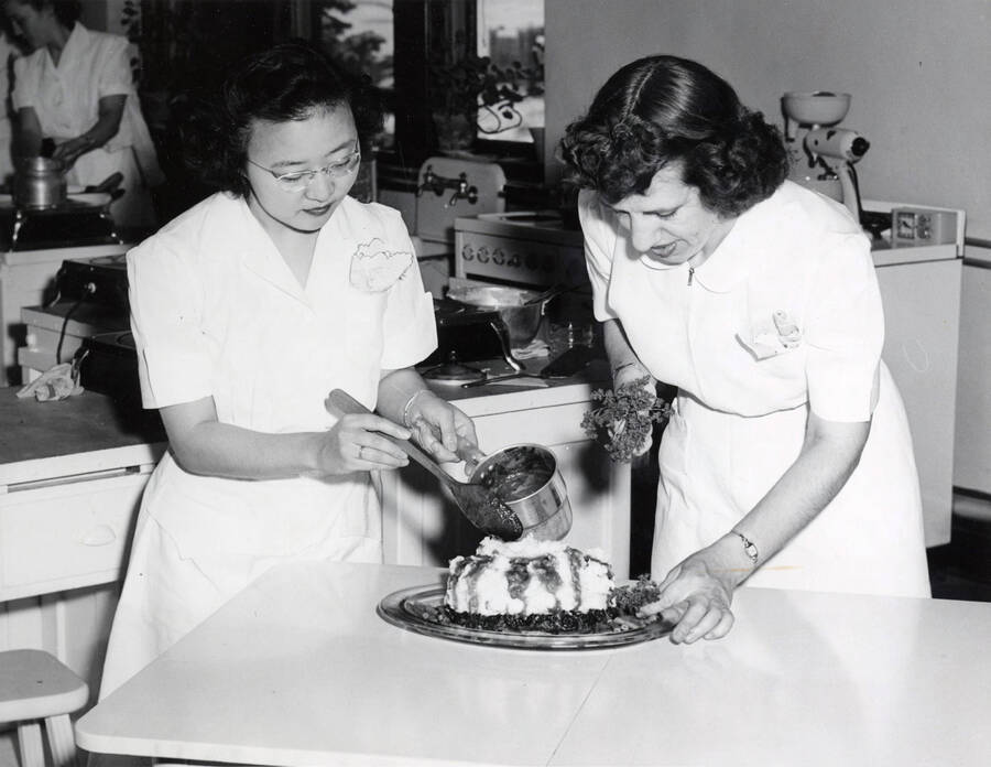 1942 photograph of Home Economics. Two students garnish a dish during cooking class. Donor: Publications Dept. [PG1_221-052]