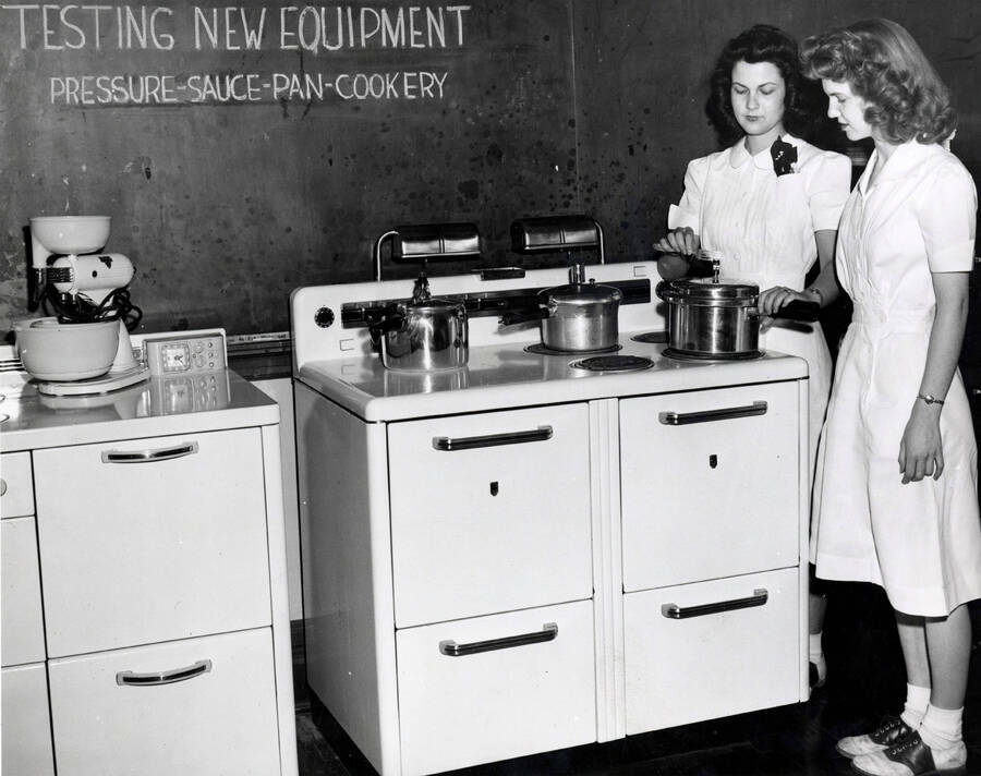 1955 photograph of Home Economics. Two students testing preasure cookers in a kitchen classroom. Donor: Publications Dept. [PG1_221-055]