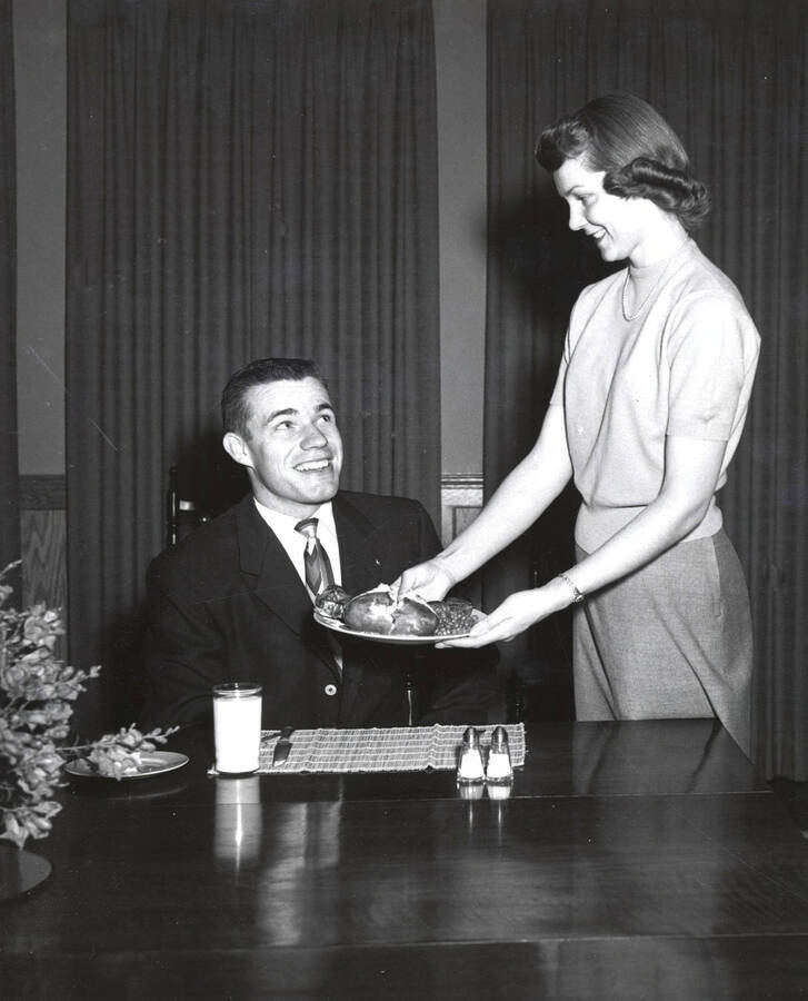 ASUI President Philip (Flip) Kleffner is served Idaho potatoes by Home Economics student Janet Campbell. University of Idaho. [221-61]