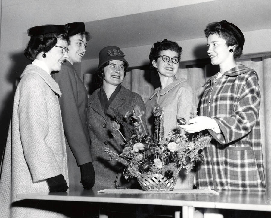 1963 photograph of Home Economics. Five students modeling coats and suits behind a flower centerpiece. Donor: Publications Dept. [PG1_221-072]