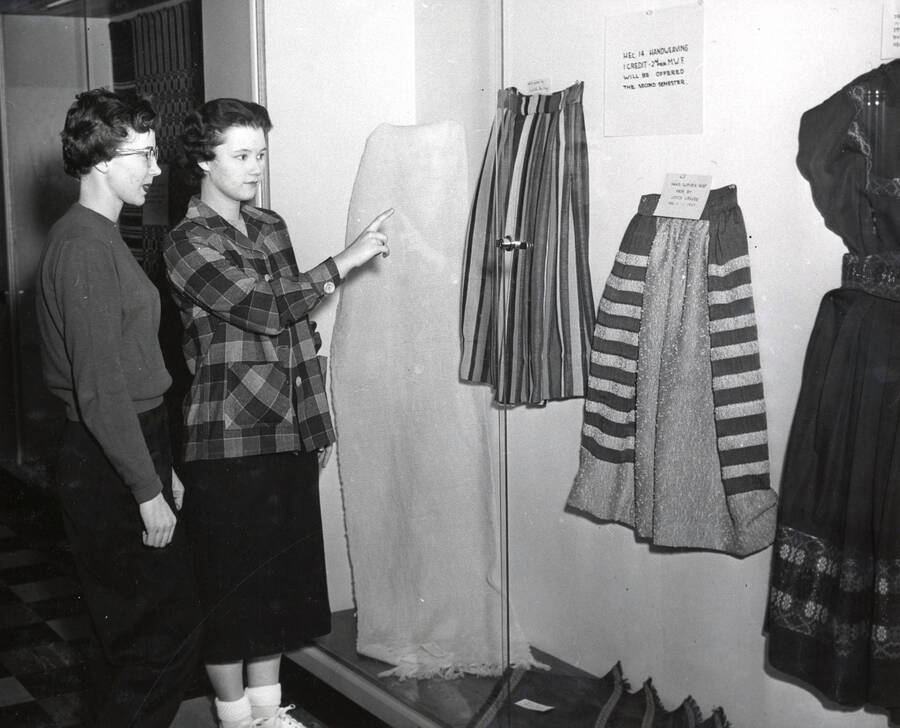 1958 photograph of Home Economics. Two women examine an exhibit of student weaving projects. Donor: Publications Dept. [PG1_221-074]