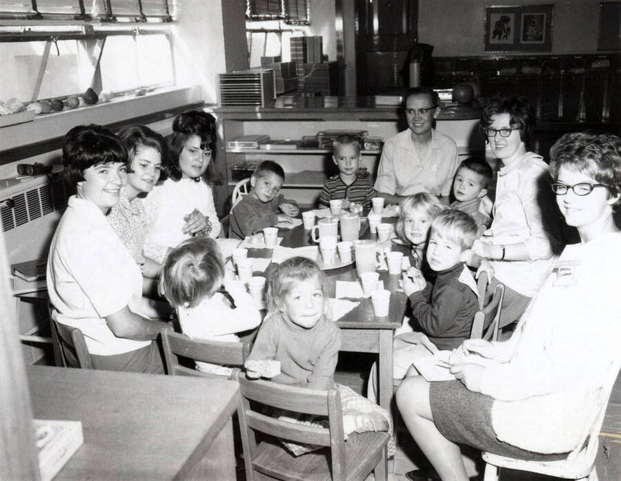 1956 photograph of Home Economics. Janice Hulsizer, Joyce Detchman, Fran Park, Vance Youmans, Ned Warnick (turned four), Mrs. Calvin Warnick, Brad Rabe, LaDessa Smelcher, Carolyn Helton, Eric Anderson, Betty Corbett, Tanys Steele, and Vicky Kappler sitting around a table during a birthday party. [PG1_221-085]