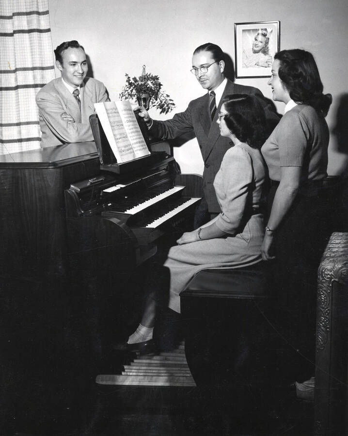 1949 photograph of Music Department. Robert McMahon, Hall Macklin, Delores Knight, Yvonne Whiting standing around the new electronic organ. Donor: Publications Dept. [PG1_222-067]