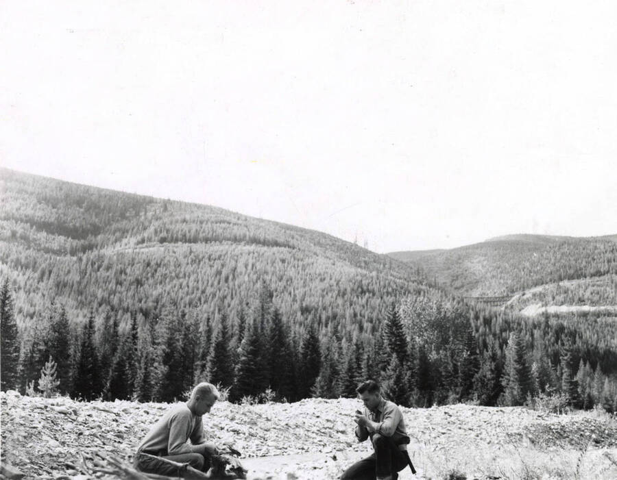 1953 photograph of College of Mines. Students sitting on a hillside during a field trip. Mountains visible in the background. [PG1_223-16]