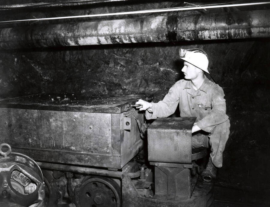 1953 photograph of College of Mines. A student operates a mine cart inside a mine. [PG1_223-22]