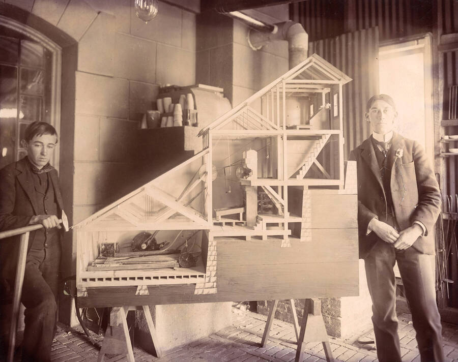 1899 photograph of College of Mines. Ralph R. Jameson, F. and Cushing Moore standing with the model of stamp and concentrate mill. [PG1_223-08]