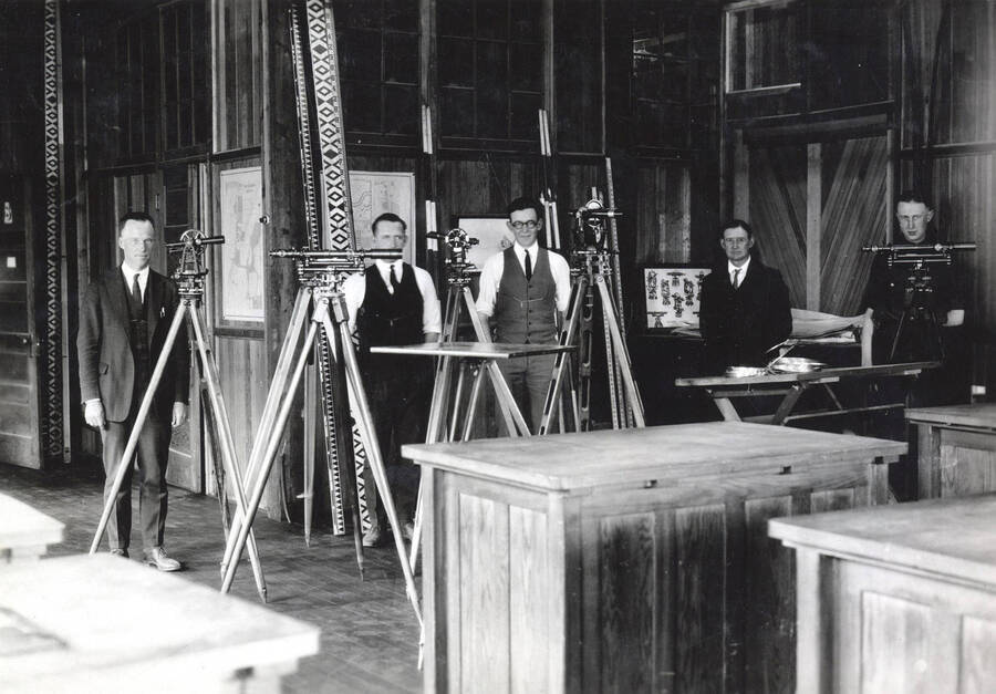 1922 photograph of College of Engineering. Students standing behind their surveying equipment in the drafting room. [PG1_224-03]