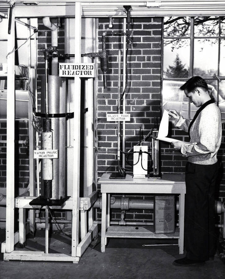 1956 photograph of College of Engineering. Fernando Vincente reading from a clipboard next to a fuildized reactor. Donor: Publications Dept. [PG1_224-34]