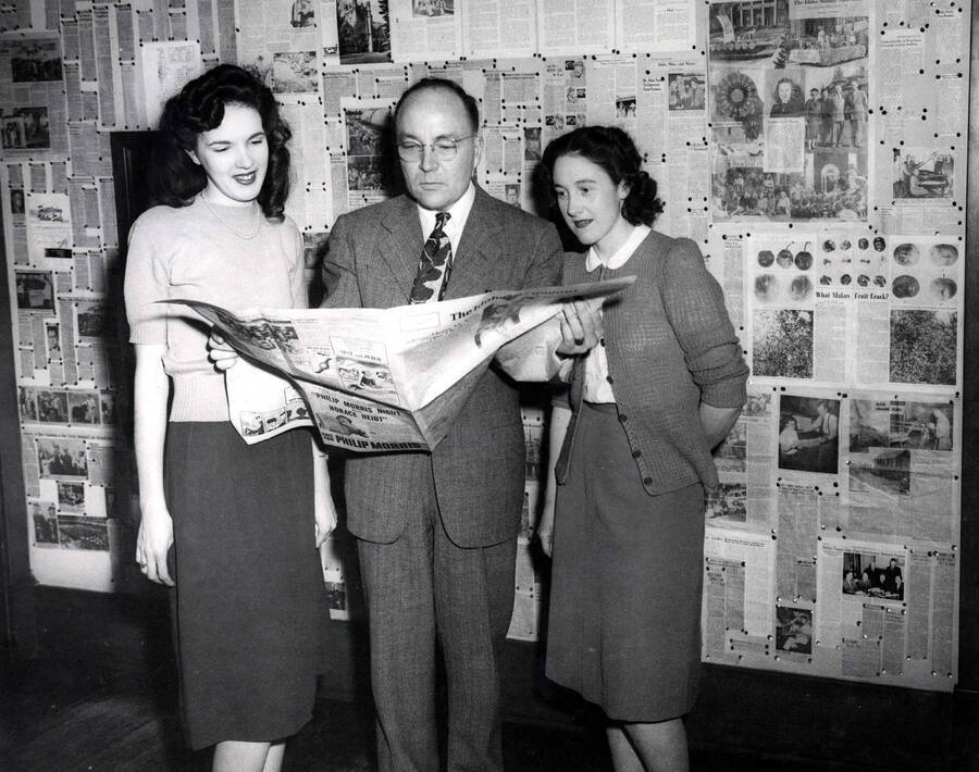 1948 photograph of Journalism. Statesman scholarship winners Joyce Hanson and Olivia Smith with Professor Paul T. Scott standing in front of a display of news papers. [PG1_226-02]