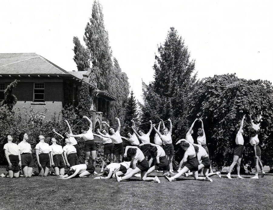 1932 photograph of Physical Education. Female students stretch and excersie outdoors. Donor: Publications Dept. [PG1_231-13]