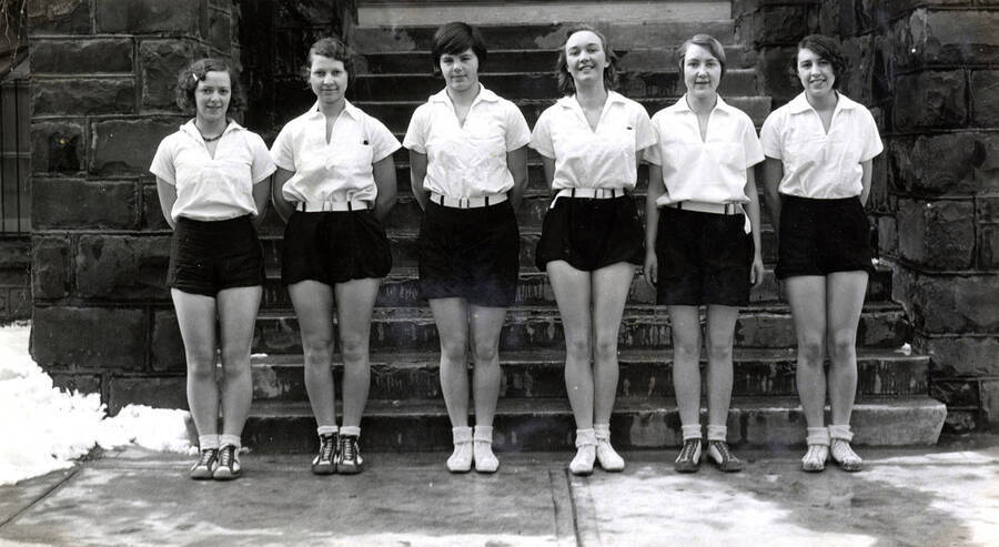 1932 photograph of Physical Education. Marjory MacVean, Vaye Miller, Rose Broemling, Evelyn Peterson, Ellen Frazier, and Mae Pugh lined up in front of the Gymnasium. [PG1_231-16]