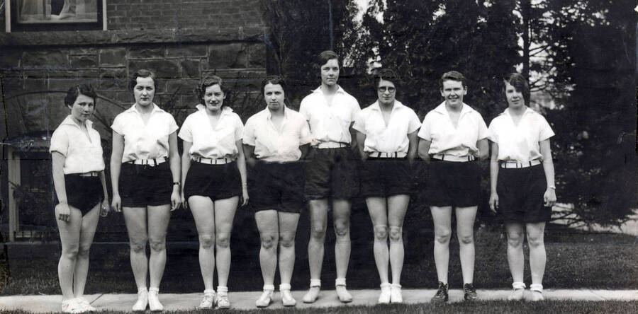 1932 photograph of Physical Education. Women's Basketball team lined up outside of the gymnasium. [PG1_231-17]