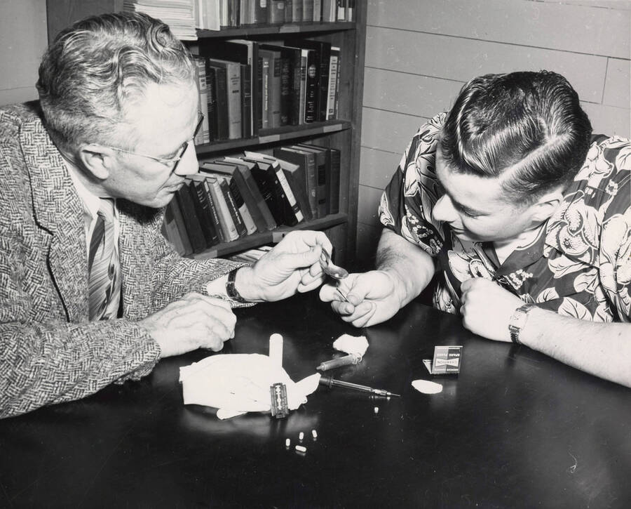 1954 photograph of Sociology Buckled. Prof. Harry C. Harmsworth and Edwin Henry Pfuhl Jr. examine drug paraphernalia. [PG1_244-01a]