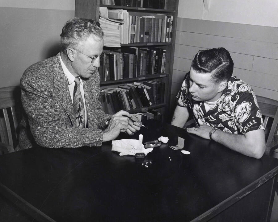 1954 photograph of Sociology Buckled. Prof. Harry C. Harmsworth and Edwin Henry Pfuhl Jr. examine drug paraphernalia [PG1_244-01c]