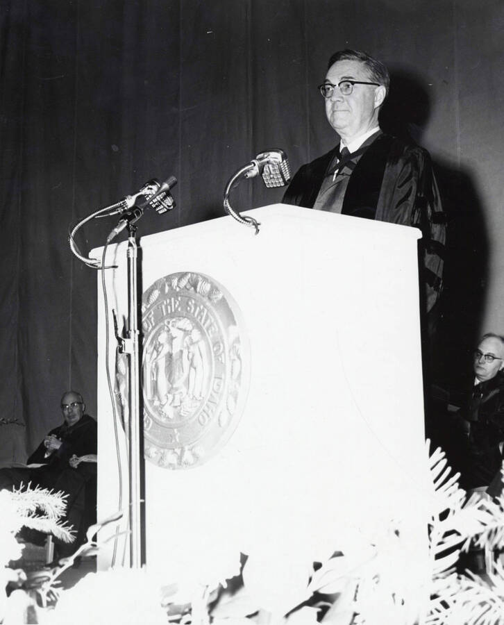 1964 photograph of 75th Anniversary. Dr. L.H. Chamberlain giving convocation address at a lectern. [PG1_246-11a]