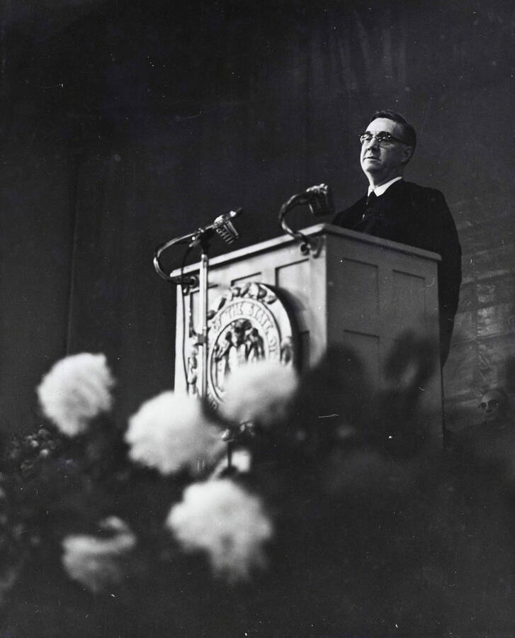 1964 photograph of 75th Anniversary. Dr. L.H. Chamberlain giving convocation address from a lectern. [PG1_246-11c]