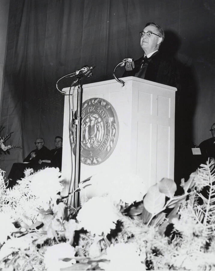 1964 photograph of 75th Anniversary. Dr. L.H. Chamberlain giving convocation address from a lectern. [PG1_246-11d]