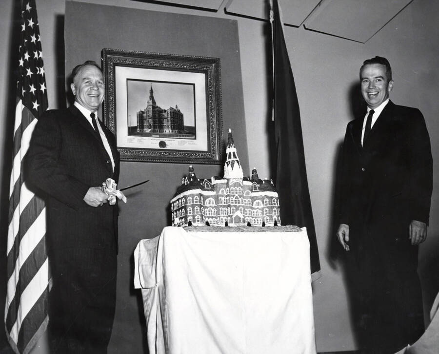 1964 photograph of 75th Anniversary. Ezra M. Hawkes and James H. Roper preparing to cut a cake shaped like the old Administration building. [PG1_246-18a]