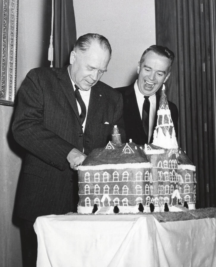 1964 photograph of 75th Anniversary. Ezra M. Hawkes and James H. Roper cuttingt a cake shaped like the old Administration building. [PG1_246-18d]