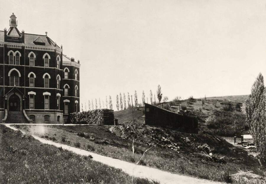 Administration Building, University of Idaho (1892-1906). Northwest corner with shed and wood-pile. [51-14a]