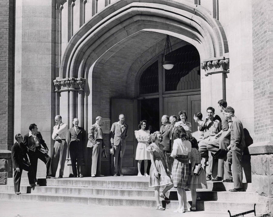 1960 photograph of University of Idaho campus scene. View of students and faculty or administrators next to administration building entrance. [PG1_006-48]