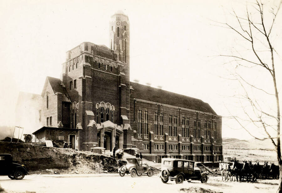 1928 photograph of Memorial Gymnasium. View of automobiles and horse drawn wagons in front. [PG1_61-32]