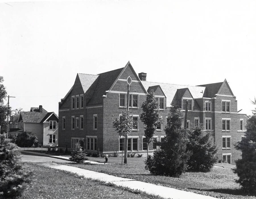 1938 photograph of Infirmary. Corner view includes the lawn, as well as parking and houses. [PG1_074-13]