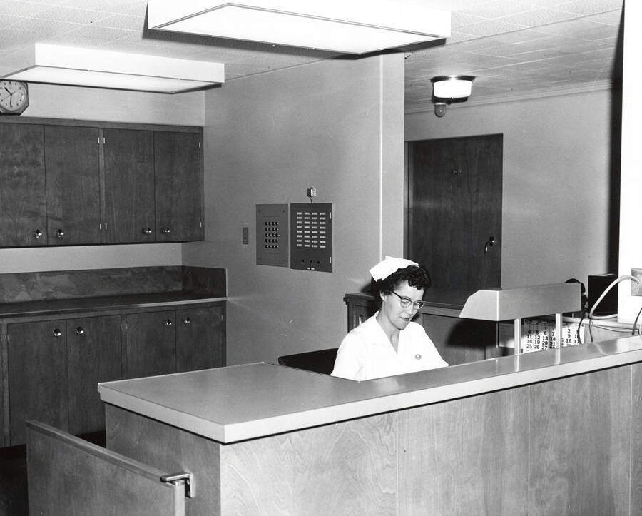 1960 photograph of Infirmary. Nurse sits at nurse's station. Donor: Publications Dept. [PG1_074-24]