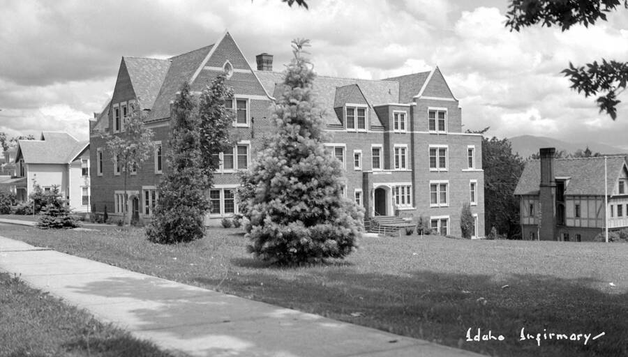 1950 photograph of Infirmary. View of the front with a fraternity visible on the right. [PG1_074-27]