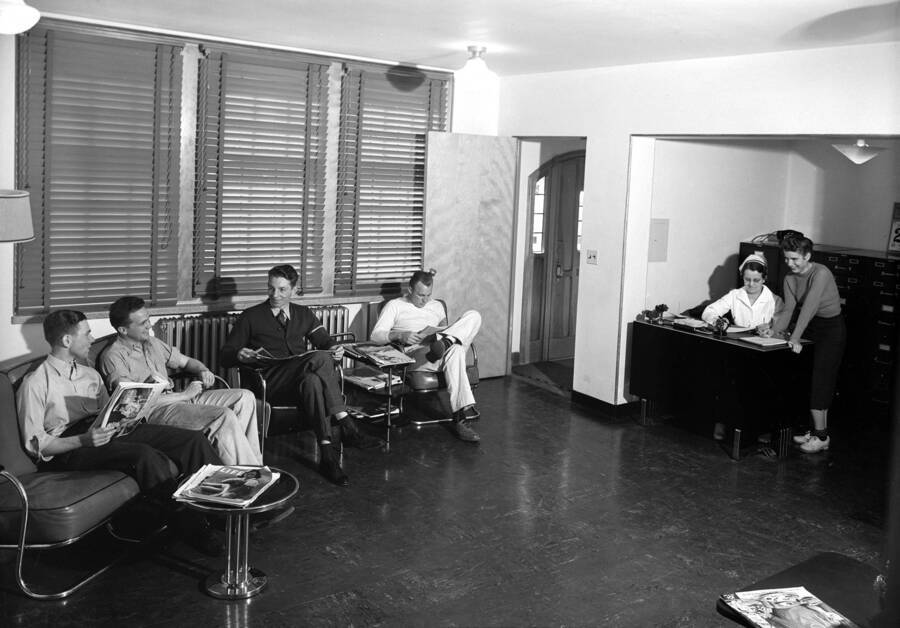 1945 photograph of Infirmary. Students in the waiting room, nurse at the desk. [PG1_074-34]