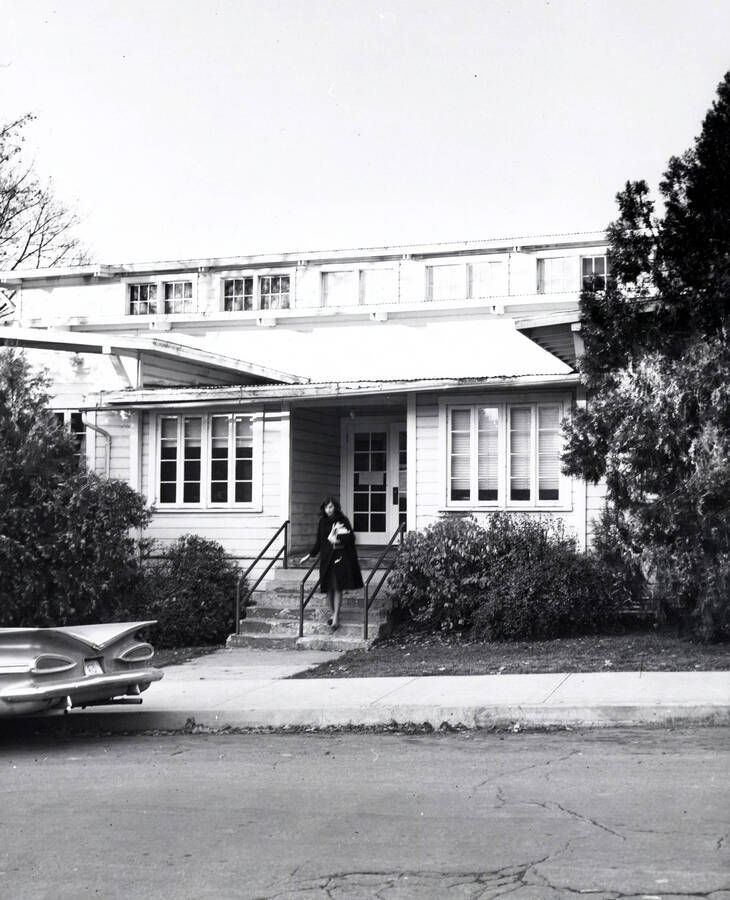 1960 photograph of University Hut. Woman exits through the main entrance. Donor: Publications Dept. [PG1_077-04]