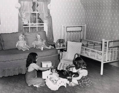 1942 photograph of Home Management House. Two children play with dolls in foreground.