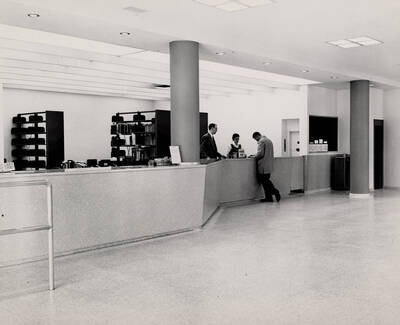 1957 photograph of the Library. Library employees helping student in foreground.
