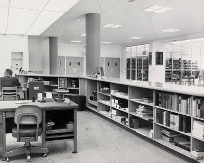 1957 photograph of the Library. A library employee sits to the left.