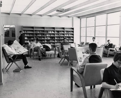 1957 photograph of the Library. Students read newspapers in foreground.