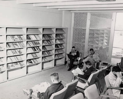 1957 photograph of the Library. Students read newspapers and magazines in foreground.