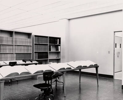 1957 photograph of the Library. Several large books are open on a table in foreground.