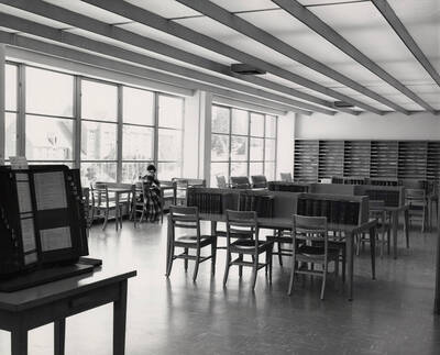 1957 photograph of the Library. Reference area with student to the left. Brink Hall can be seen in background.