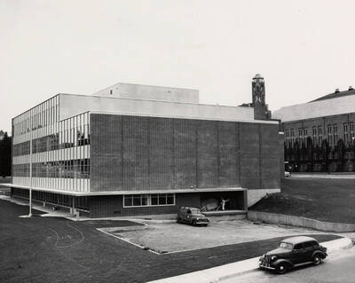 1957 photograph of the Library under construction. Automobiles in foreground, Memorial Gym to the right. Donor: Publications Dept.