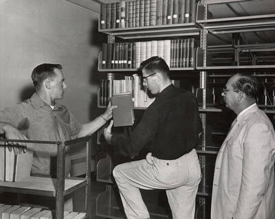 1957 photograph of the Library. Moving books into the new library, left to right: Lee Shellman, Mike McQuade, Edmond Gnoza. Donor: Publications Dept.
