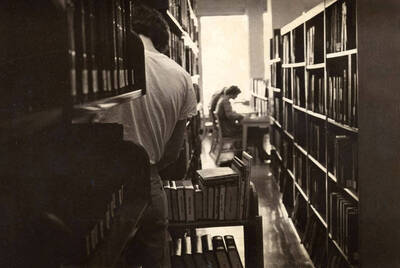 1978 photograph of the Library. A library employee shelves books while students study in the background.